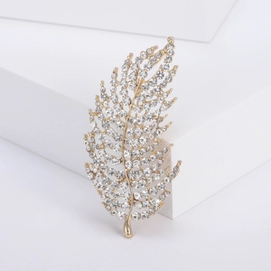 Detail of a golden leaf brooch featuring sparkling crystals on a white geometric stand