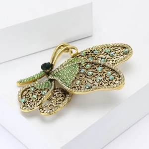 Vintage gold butterfly brooch with green rhinestones on white display steps