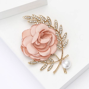 Broche fleur en tissu rose avec feuille dorée et perle sur un fond blanc épuré