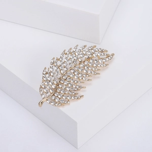 Elegant gold hollow leaf brooch with sparkling crystals on minimalist white background
