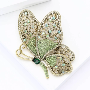 Macro detail of vintage gold butterfly brooch featuring emerald green rhinestones and filigree