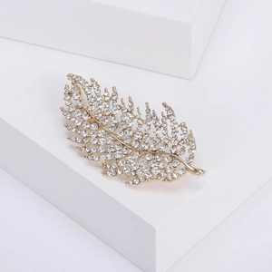 Close-up of elegant gold feather brooch with sparkling rhinestones on white block