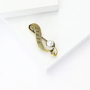 Macro detail of a vintage gold musical note brooch featuring a central white pearl inlay