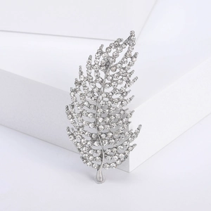 Macro shot of silver hollow leaf brooch with sparkling crystals on white geometric stand