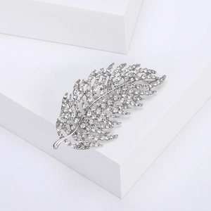 Detailed close-up of a silver leaf brooch featuring shimmering white rhinestones in a modern style