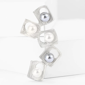 Close-up of matte silver square brooch with embedded pearls on a white geometric background