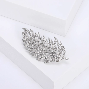 Elegant silver feather brooch with sparkling crystals on minimalist white background