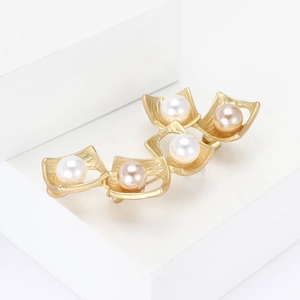 Golden matte alloy square brooch with five pearls and brushed texture on white steps