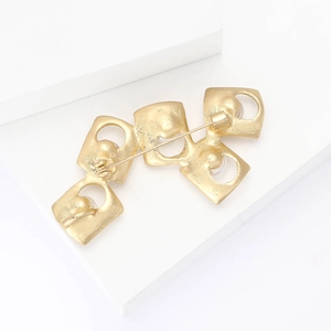 Detail of matte gold square brooch with floral texture and secure safety pin closure