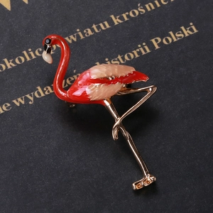 Detail shot of golden flamingo brooch with red and pink enamel on a textured background
