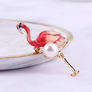Detailed close-up of a pink enamel flamingo brooch with a central pearl on a white tray