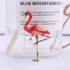 Detailed close-up of flamingo brooch with red enamel and a large pearl on golden metal