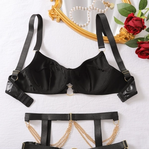 Detail von schwarzem Satin-Dessous-Set mit goldenen Ketten und Strapsgürtel auf weißem Grund