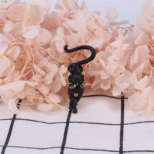 Detailed close-up of a black cat brooch with green gem eyes and golden metallic accents