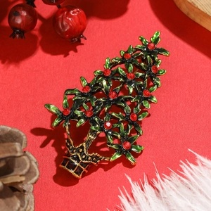 Broche de sapin de Noël festive en émail vert et strass rouges sur fond rouge de vacances