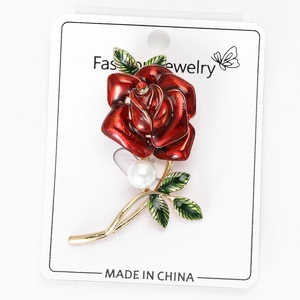 Detail of red rose brooch with green enamel leaves, gold stems and a white pearl accent