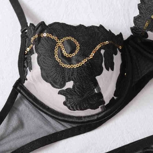 Detail von Blumenstickerei mit goldenen Pailletten und schwarzer Spitze auf transparentem BH