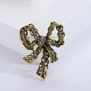 Vintage gold alloy bow brooch featuring brown rhinestones on a white display block