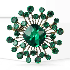 Macro shot of vintage sunburst brooch featuring emerald-cut green crystal in gold setting