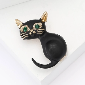 Broche chat en émail noir avec yeux en pierres vertes et détails dorés sur socle blanc