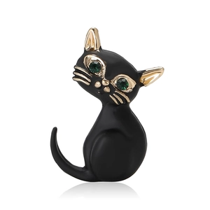 Broche chat en émail noir avec yeux en pierres vertes et détails dorés sur fond blanc