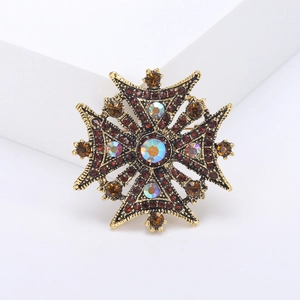 Vintage golden Maltese cross brooch with brown crystals and AB rhinestones on a white stand