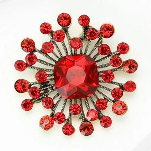 Close-up of vintage sunburst brooch featuring a large red gemstone and golden rays