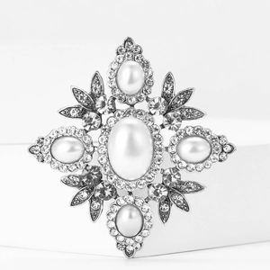 Baroque vintage alloy brooch with large oval pearl and sparkling rhinestones on white stand