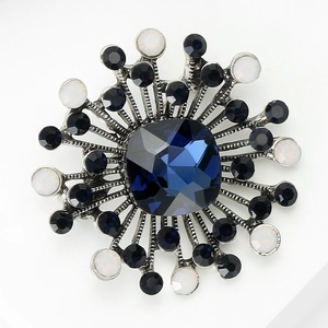 Detailed macro view of vintage sunburst brooch with deep blue faceted gemstone and rhinestones