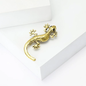 Macro detail of golden gecko lizard brooch with vintage texture and black gem eyes