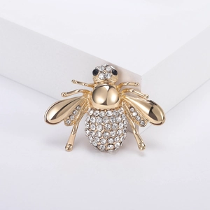 Élégante broche abeille dorée ornée de strass blancs et yeux en pierres noires sur fond blanc