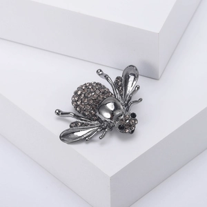 Détail macro d'une broche abeille sertie de cristaux sur un socle géométrique blanc