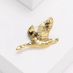 Gros plan d'une broche oiseau dorée montrant l'alliage vintage et le fermoir épingle