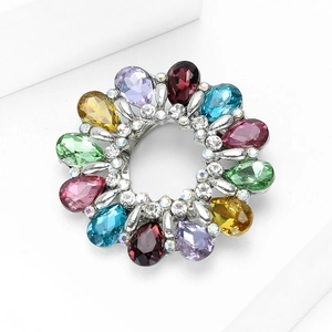 Détail d'une broche couronne avec cristaux colorés en goutte sur un socle blanc