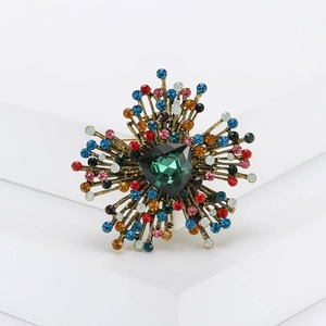 Detailed macro view of vintage gold sunburst brooch with a green crystal and colorful rhinestones