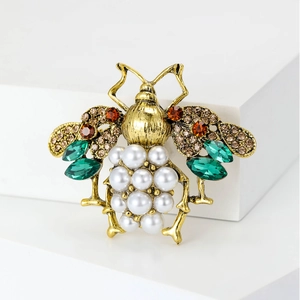 Macro detail of vintage bee brooch with pearls, green crystals, and gold-tone alloy plating