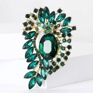 Macro detail of vintage gold brooch with large emerald green stone and sparkling rhinestones