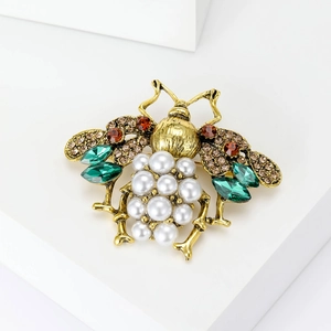 Detailed macro shot of vintage bee brooch with pearls and green crystals on gold metal