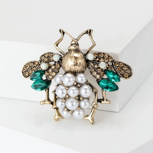 Close-up of vintage bee brooch featuring pearl abdomen and emerald green gemstones