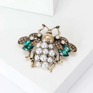 Macro detail of bee brooch with pearls, champagne crystals and emerald accents
