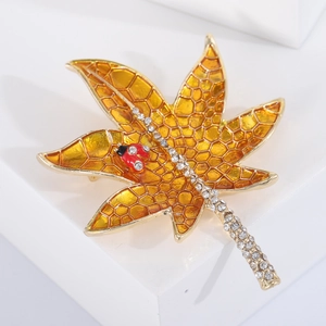 Elegant maple leaf brooch with crystal-studded stem and small ladybug detail on white stand