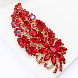 Vintage gold brooch with red floral crystals and bow detail on a white platform