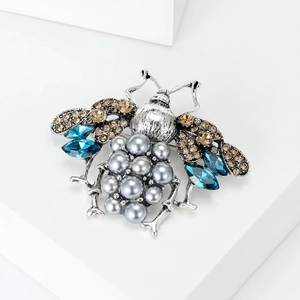 Detailed macro view of vintage bee brooch with blue crystals and grey faux pearls