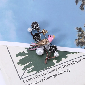 Vintage bird and flower brooch featuring pearls, crystals, and enamel on a nature branch