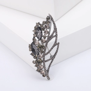 Leaf brooch in gunmetal finish with smoky grey rhinestones on a white pedestal