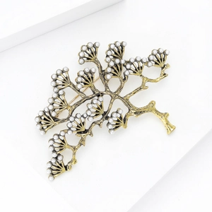 Détail macro d'une broche branche de pin dorée vintage avec perles sur socle blanc