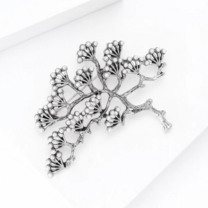 Gros plan d'une broche branche de pin argentée vintage avec perles sur socle blanc