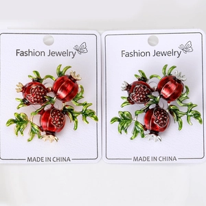 Detail view of red enamel pomegranate brooches in gold and silver finish on display cards