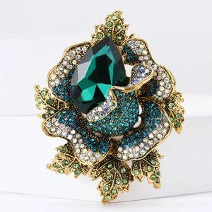 Vintage floral brooch with emerald rhinestone center and blue crystals on white stand