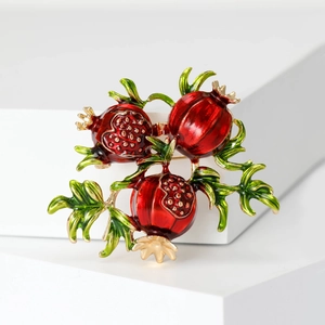 Detailed view of red enamel pomegranate brooch with golden seeds on white pedestal